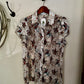 Floral patterned shirt hanging on a hook against a white wall.