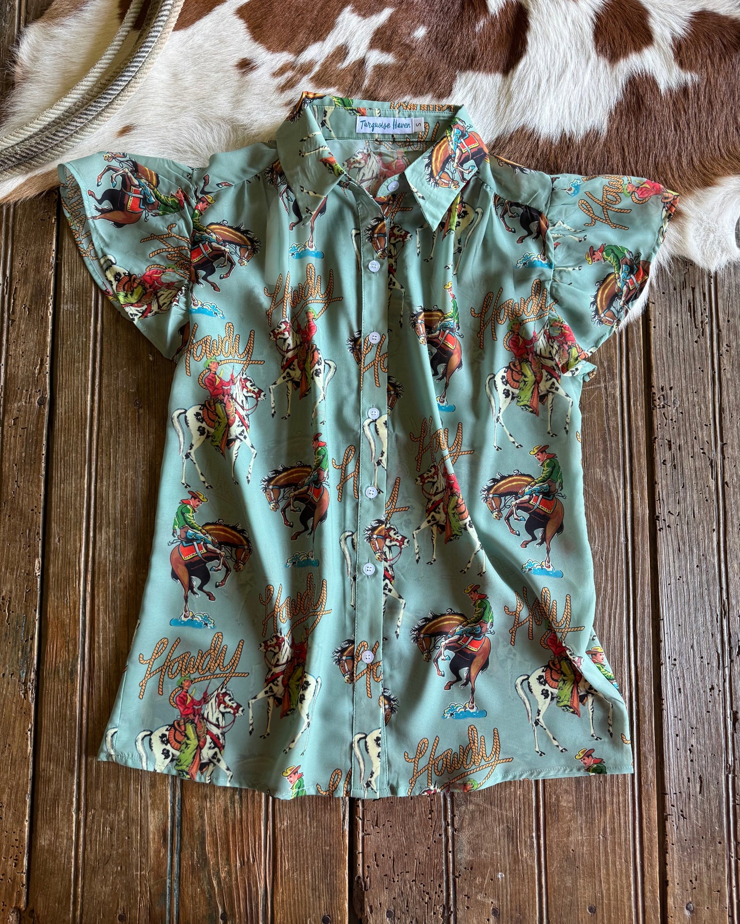 Turquoise blouse with cowboy pattern on a wooden surface