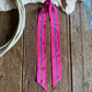 pink ribbon scarf with a pattern on a wooden surface next to a cowhide and rope.