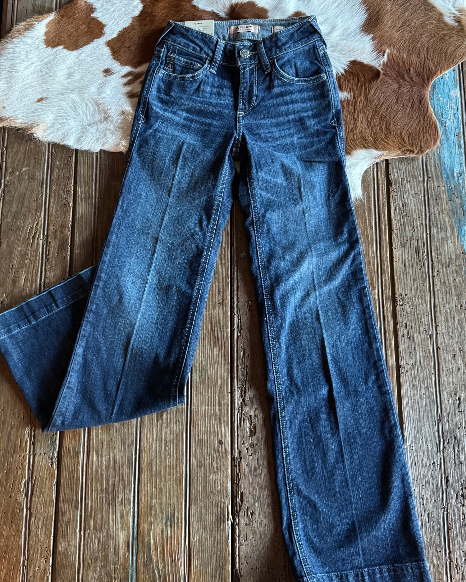 Blue jeans on a wooden surface with a cowhide rug in the background