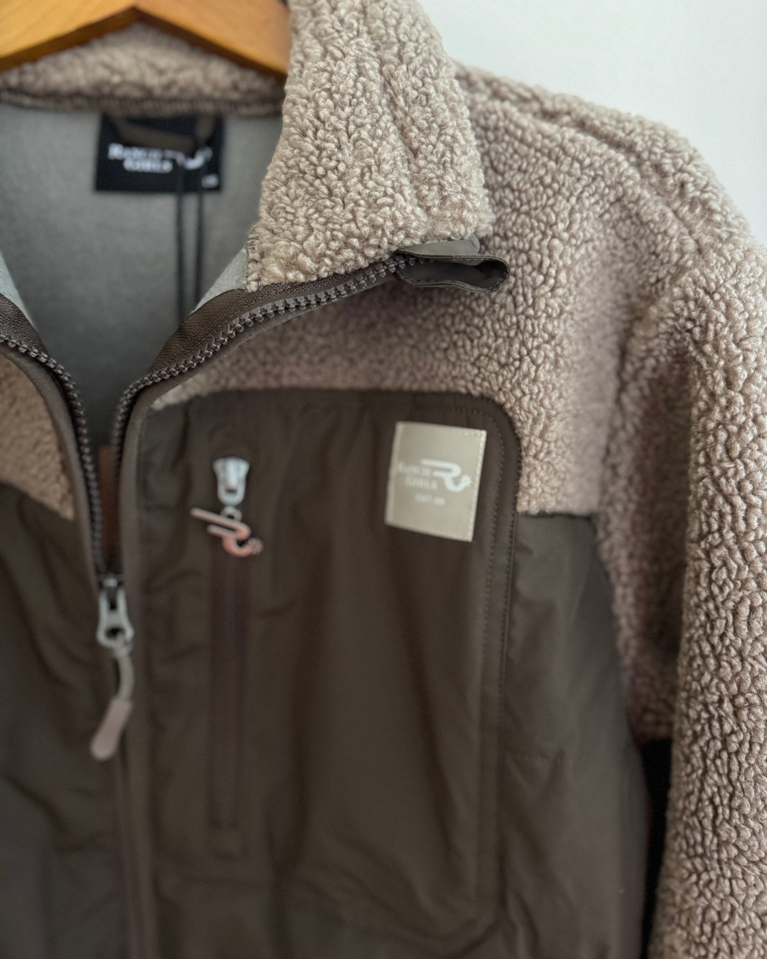Brown fleece jacket with a visible brand logo on a hanger against a white background