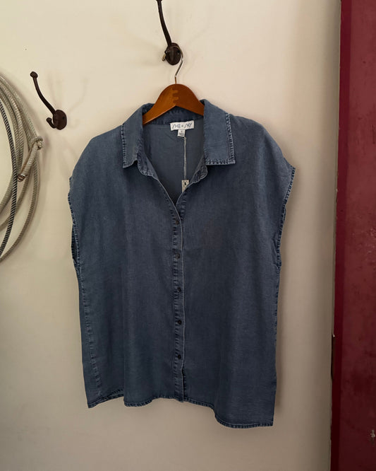 Blue denim shirt on a hanger against a beige wall.