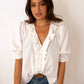 Woman wearing a white blouse and blue jeans sitting on a stool against a plain background