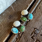 A pair of silver-toned stud earrings with oval turquoise-blue, green, and cream cabochon stones, displayed on a rustic wooden surface next to a white faux fur trim.