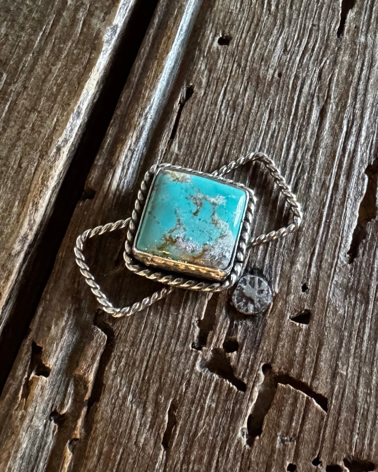 A square turquoise and silver twilly slide resting on a weathered, rustic wooden surface.