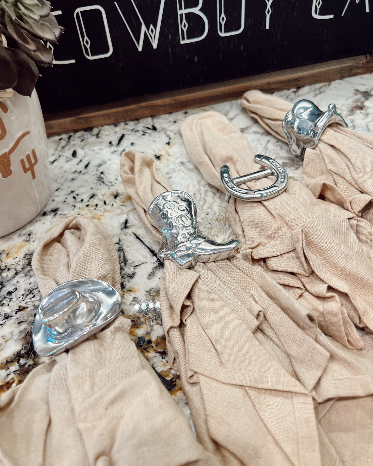Beige napkins with silver cowboy boot and hat decorations on a marble surface.