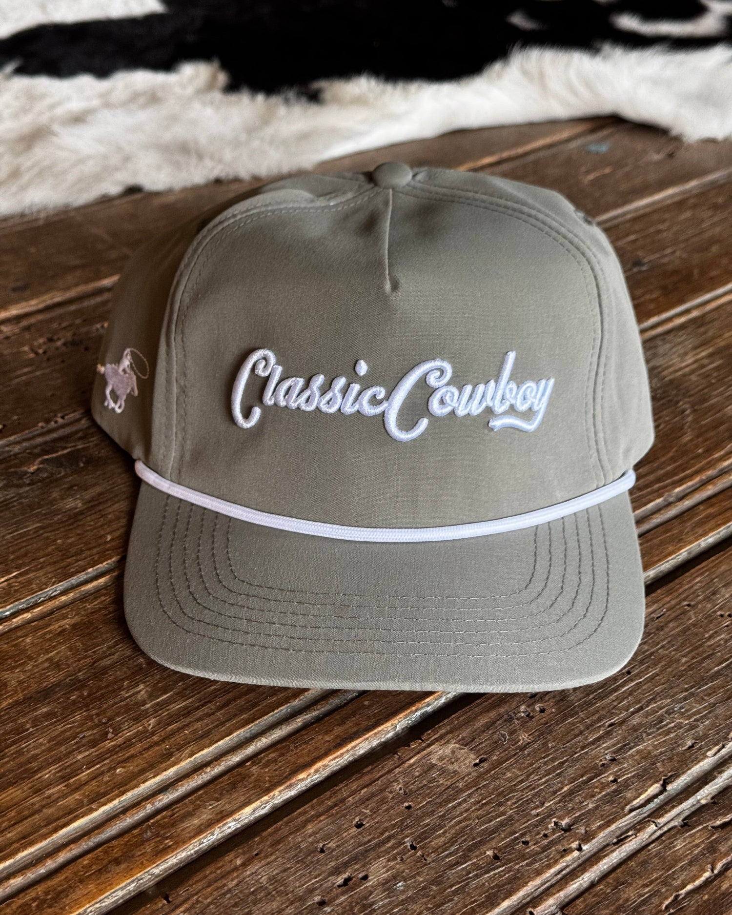 Green cap with 'Classic Cowboy' text on a wooden surface with cowhide rug in the background