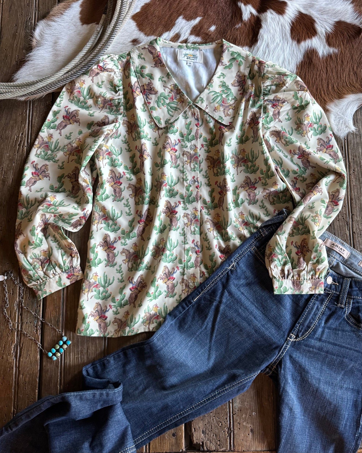 Retro cowgirl and cactus print blouse and jeans on a wooden surface with cowhide rug