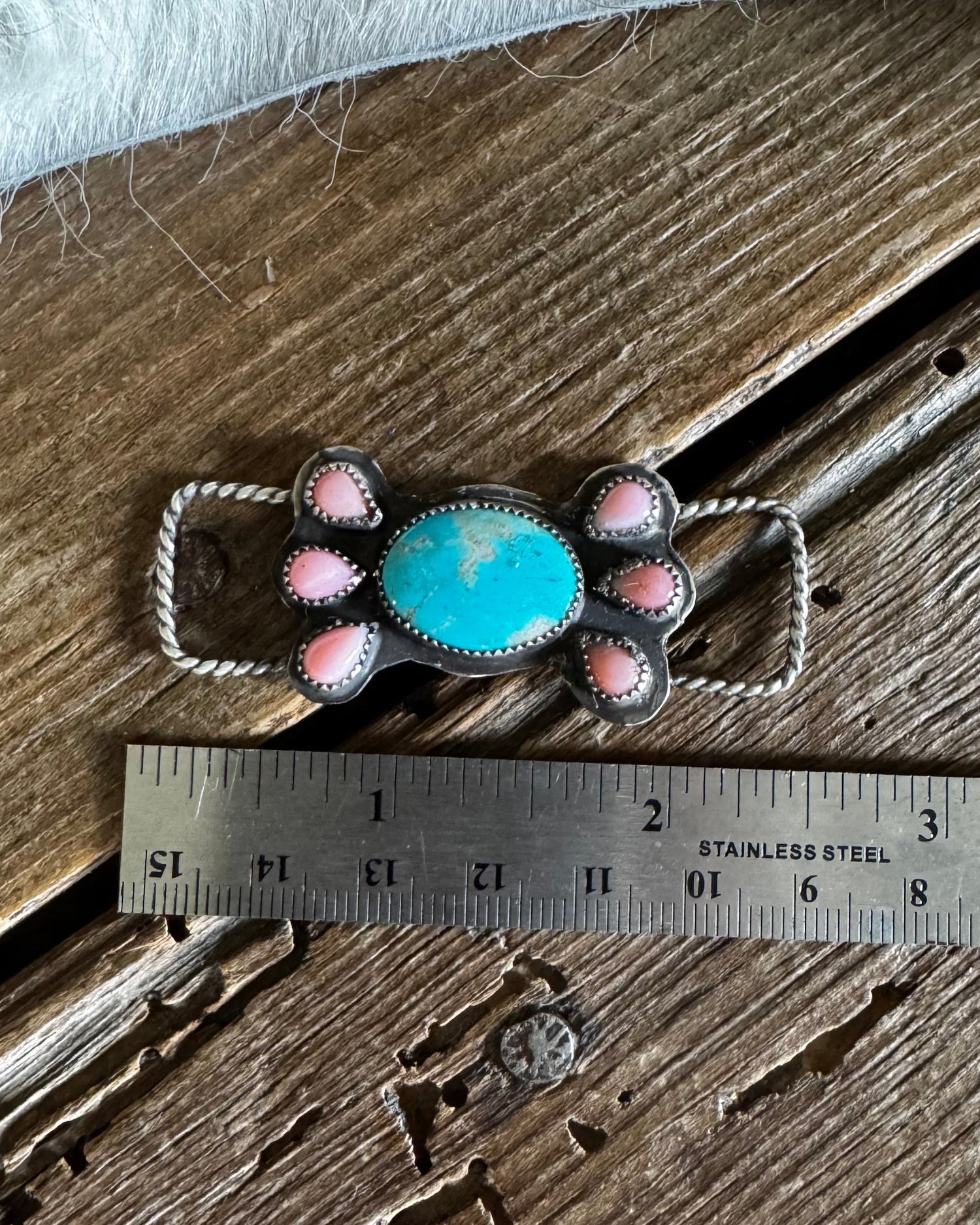 Turquoise and pink conch twilly slide on wooden background with ruler to show size