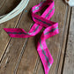 Pink ribbon scarf with geometric patterns on a wooden surface