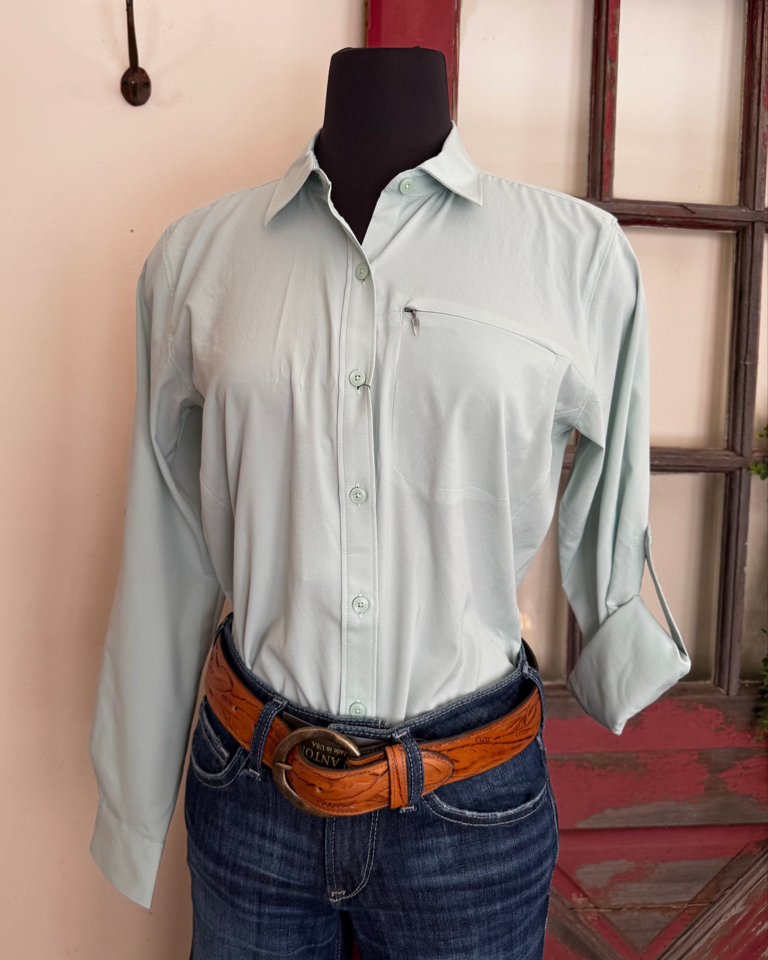 Person wearing a light green shirt and blue jeans with a brown belt, standing indoors.
