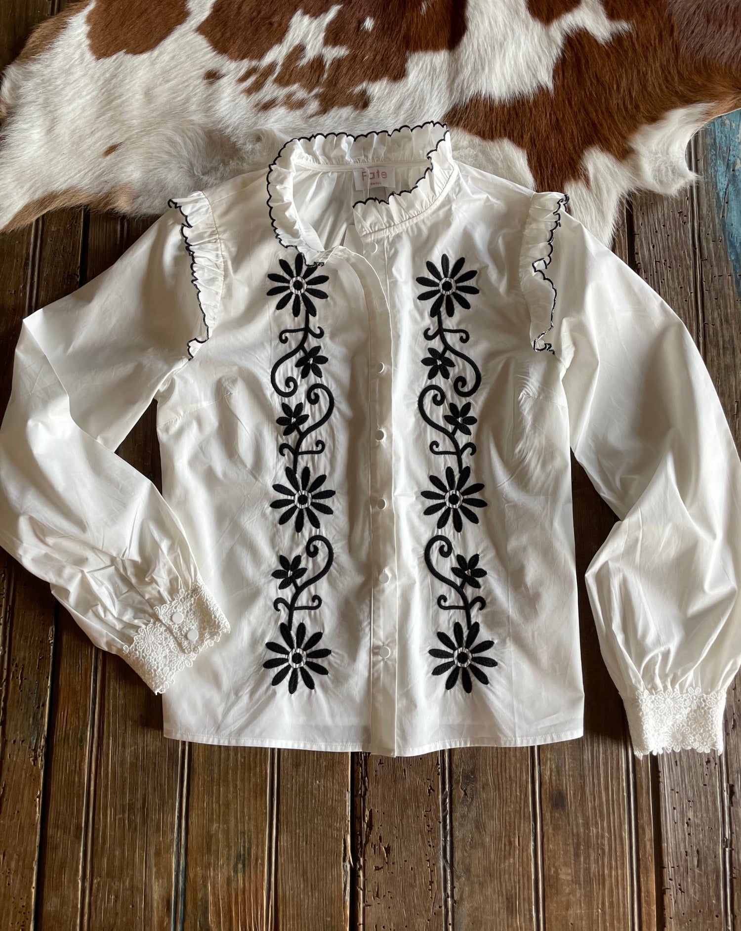 Flat lay of white blouse with black embroidery and ruffle detail