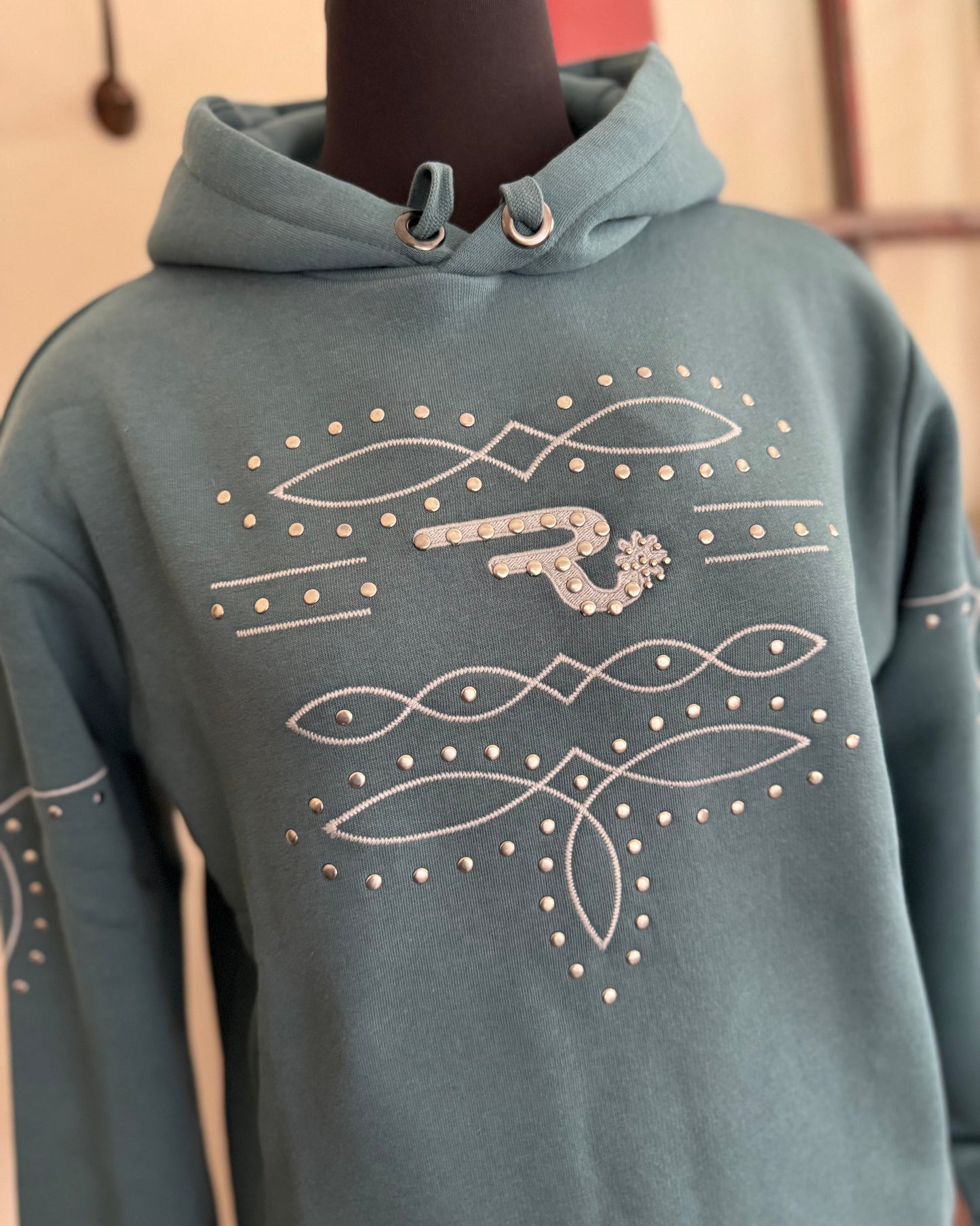 blue hoodie with decorative patterns on a mannequin against a neutral background