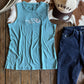 Blue tank top, blue jeans, and beige cap on a wooden surface with cowhide rug