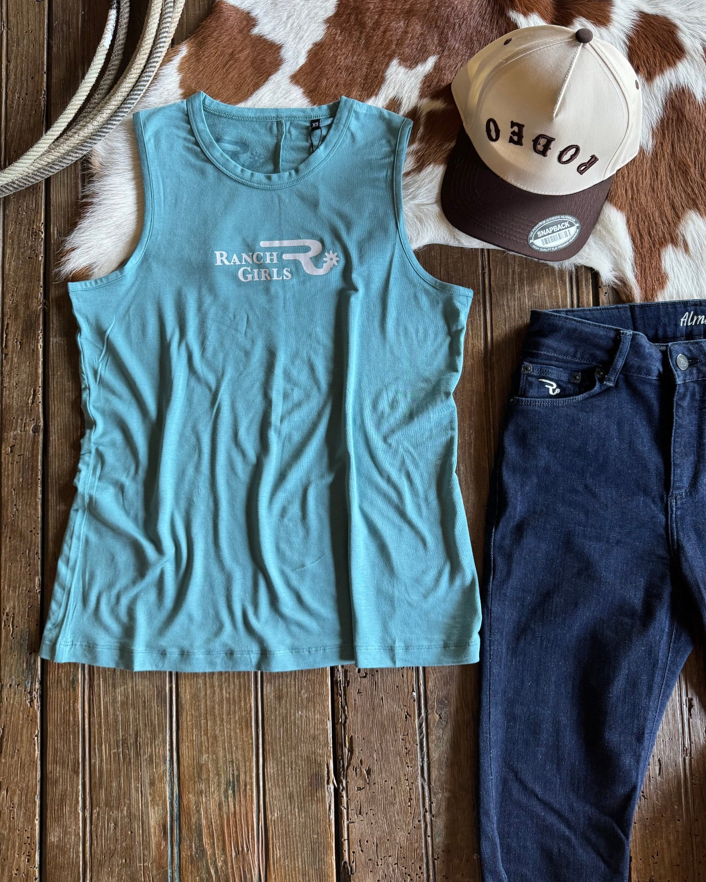 Blue tank top, blue jeans, and beige cap on a wooden surface with cowhide rug
