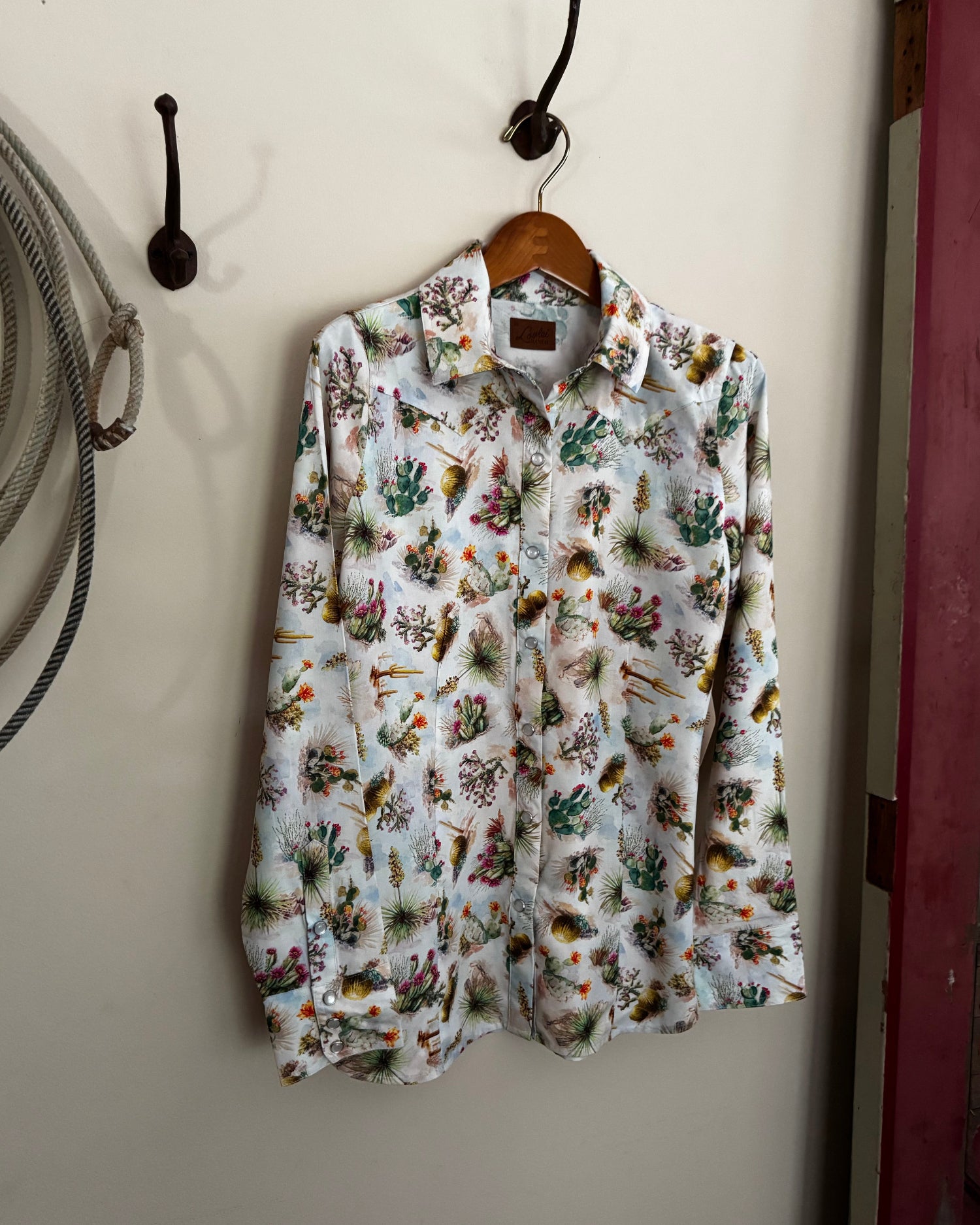Floral patterned shirt hanging on a hook against a white wall.