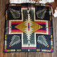 Colorful patterned scarf on a wooden surface with cowhide rug and hat in the background