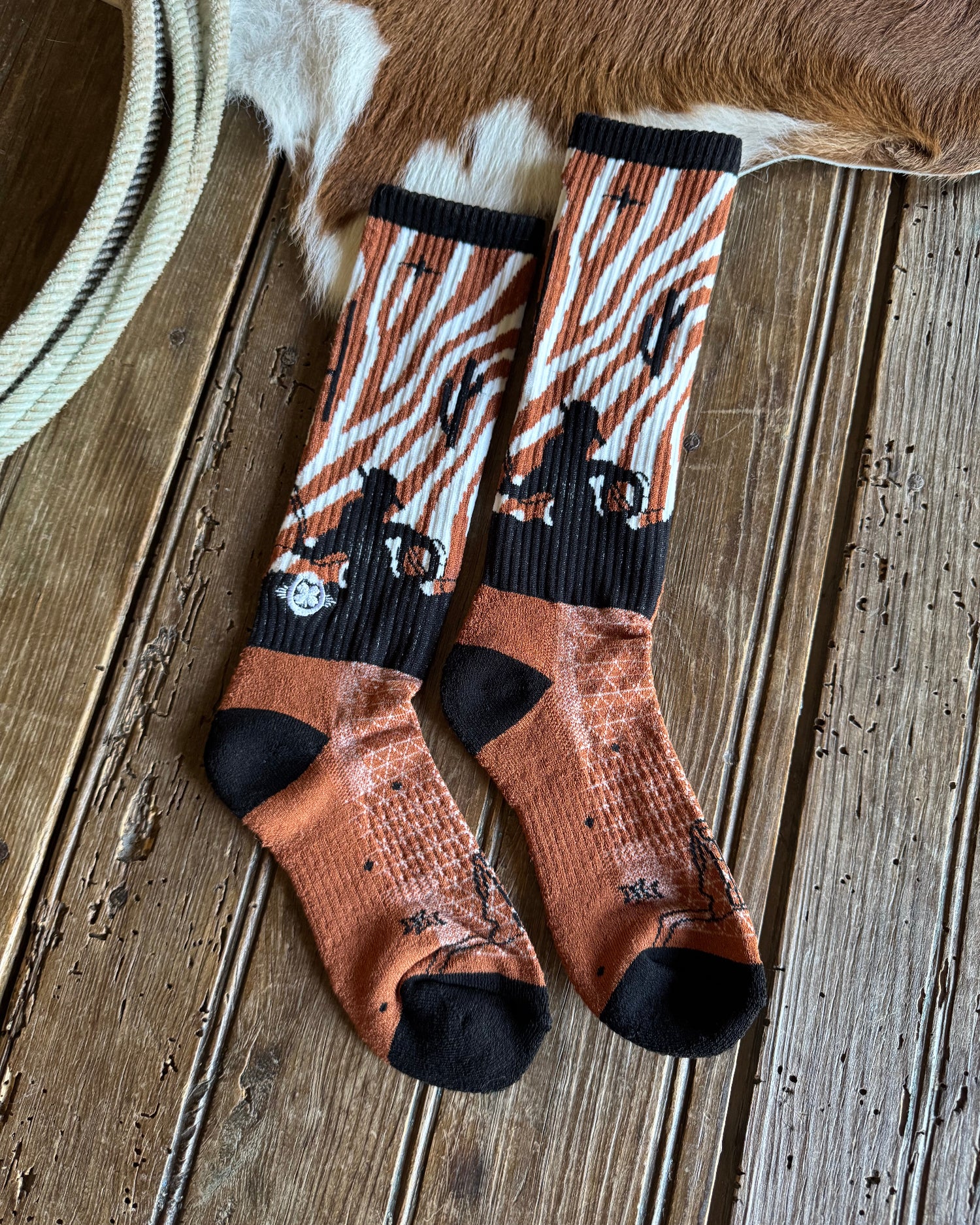 Pair of patterned socks on a wooden surface with a cowhide rug.