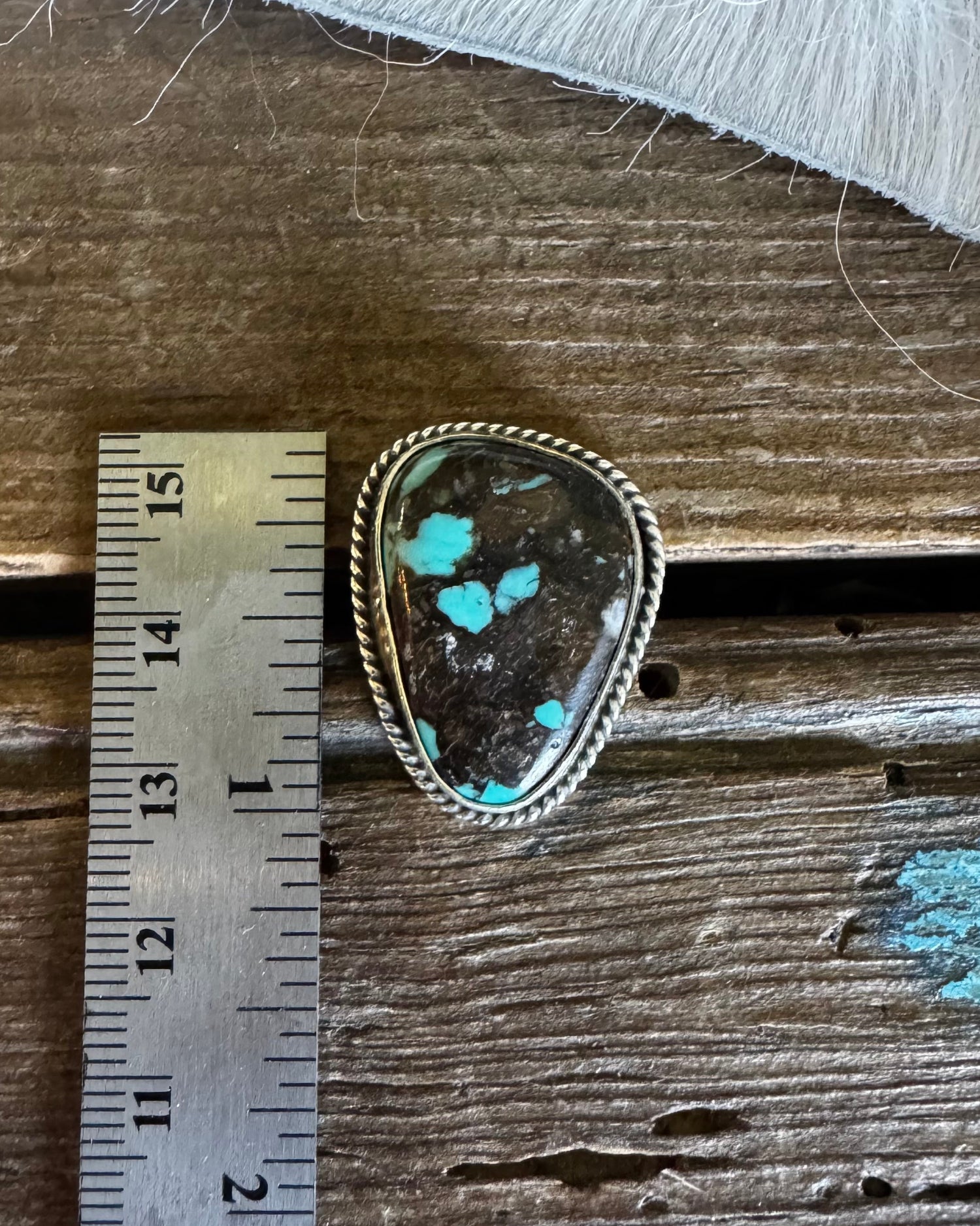 Turquoise stone in a gold frame on a wooden surface with a ruler for scale.