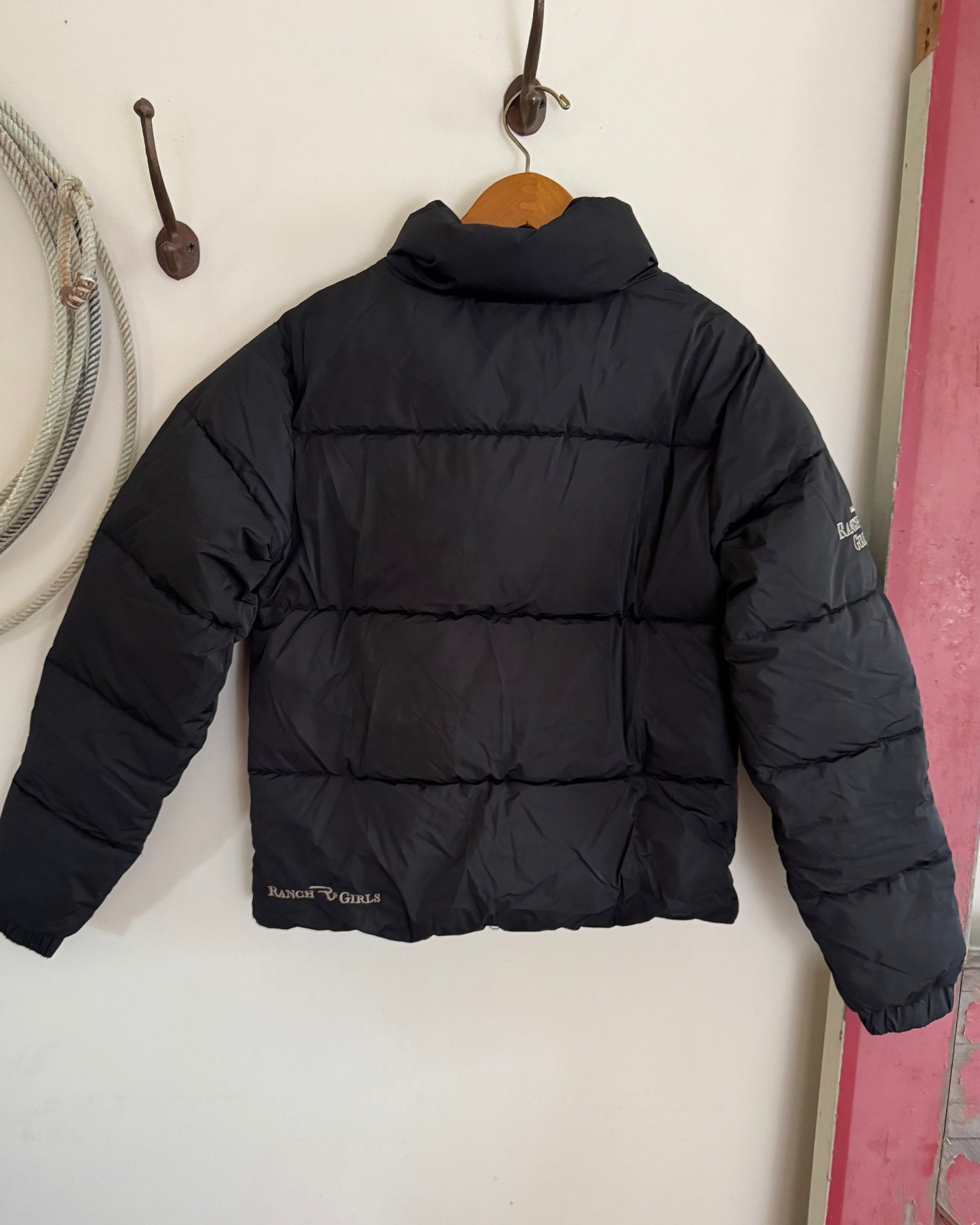 Black puffer jacket on a white surface with a pink object in the background