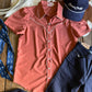 Pink shirt, navy pants, and blue cap on a wooden surface with cowhide rug