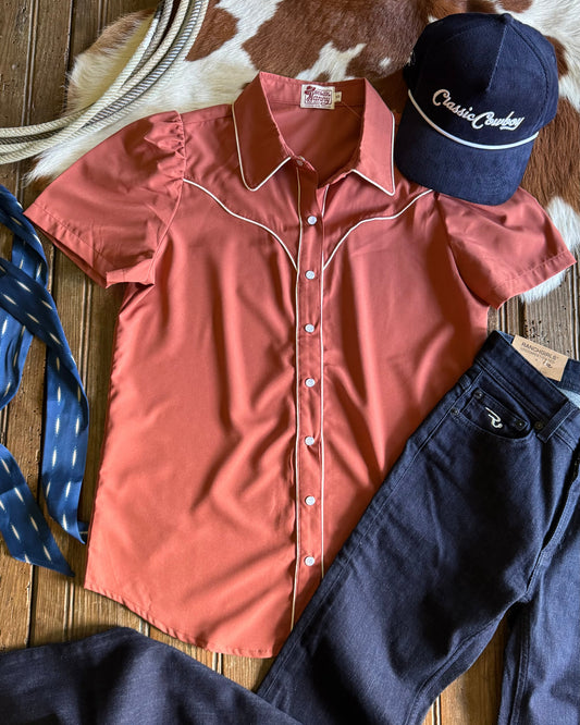 Pink shirt, navy pants, and blue cap on a wooden surface with cowhide rug