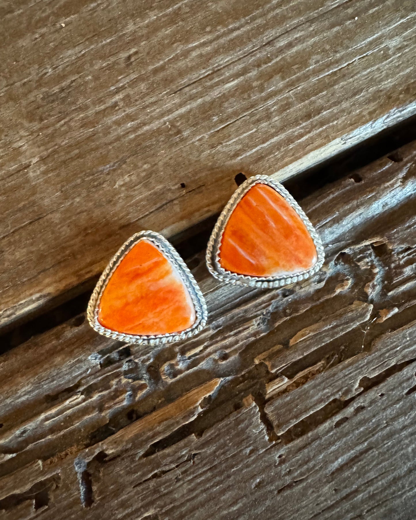 Orange triangular earrings with silver borders on a wooden surface