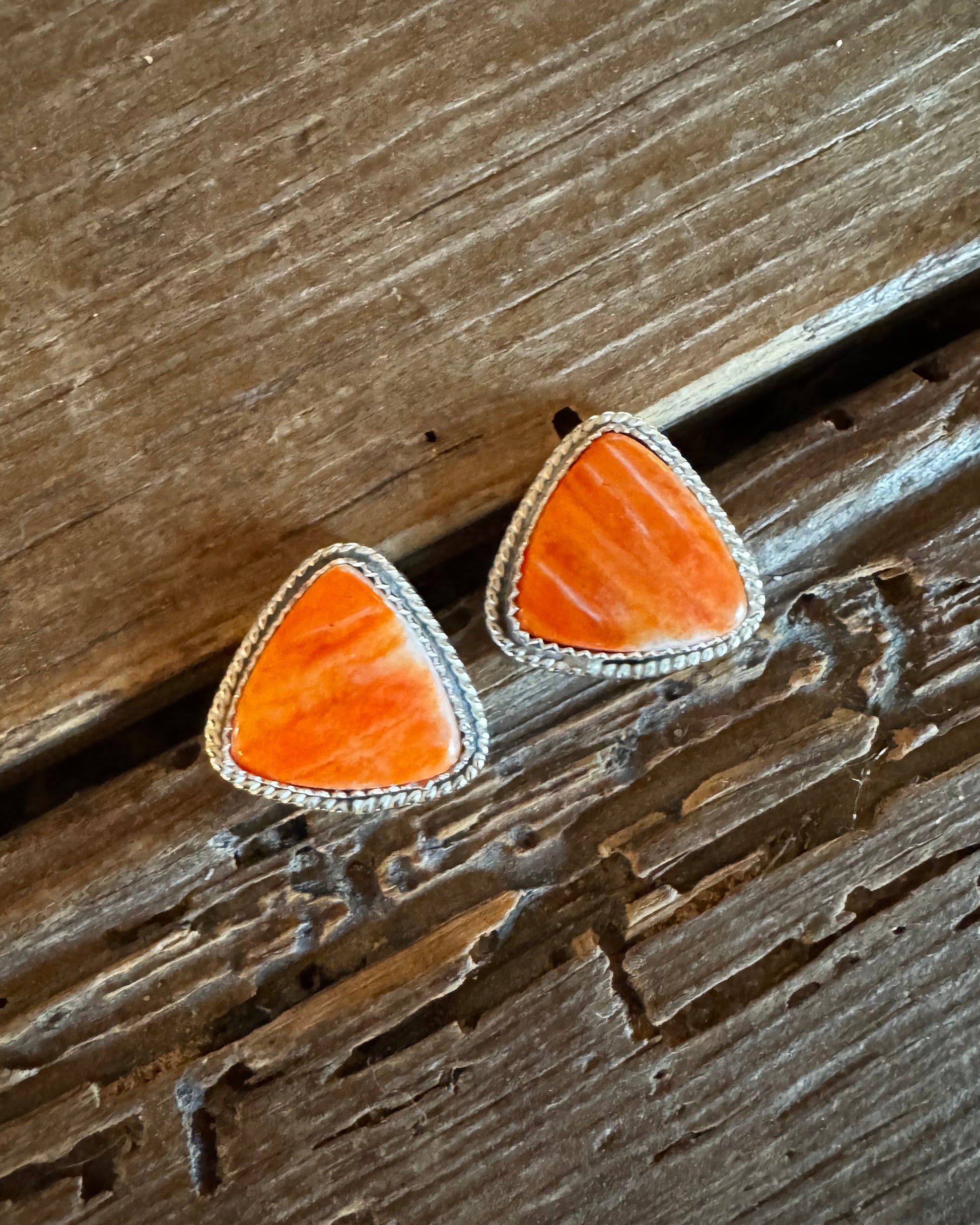 Orange triangular earrings with silver borders on a wooden surface
