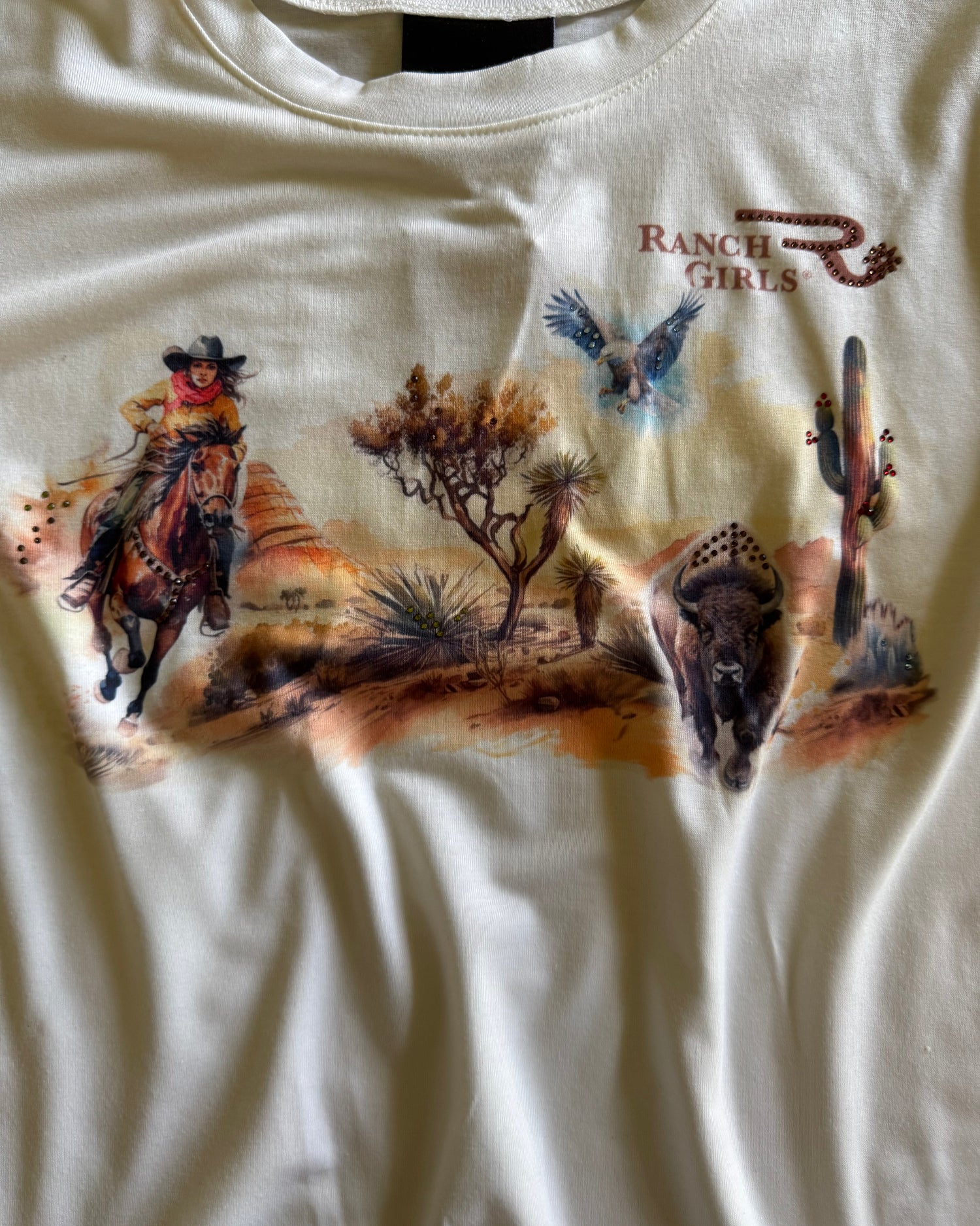 White t-shirt with desert-themed graphic design featuring a horse, cactus, and birds.