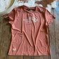 Pink t-shirt with 'Ranch Girls' logo on a wooden surface next to a cowhide rug