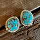 Turquoise stone earrings with gold accents on a wooden surface