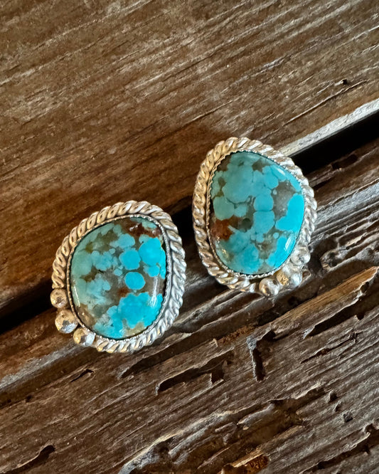 Turquoise stone earrings with gold accents on a wooden surface