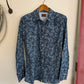 Blue patterned shirt hanging on a wooden hanger against a white wall.
