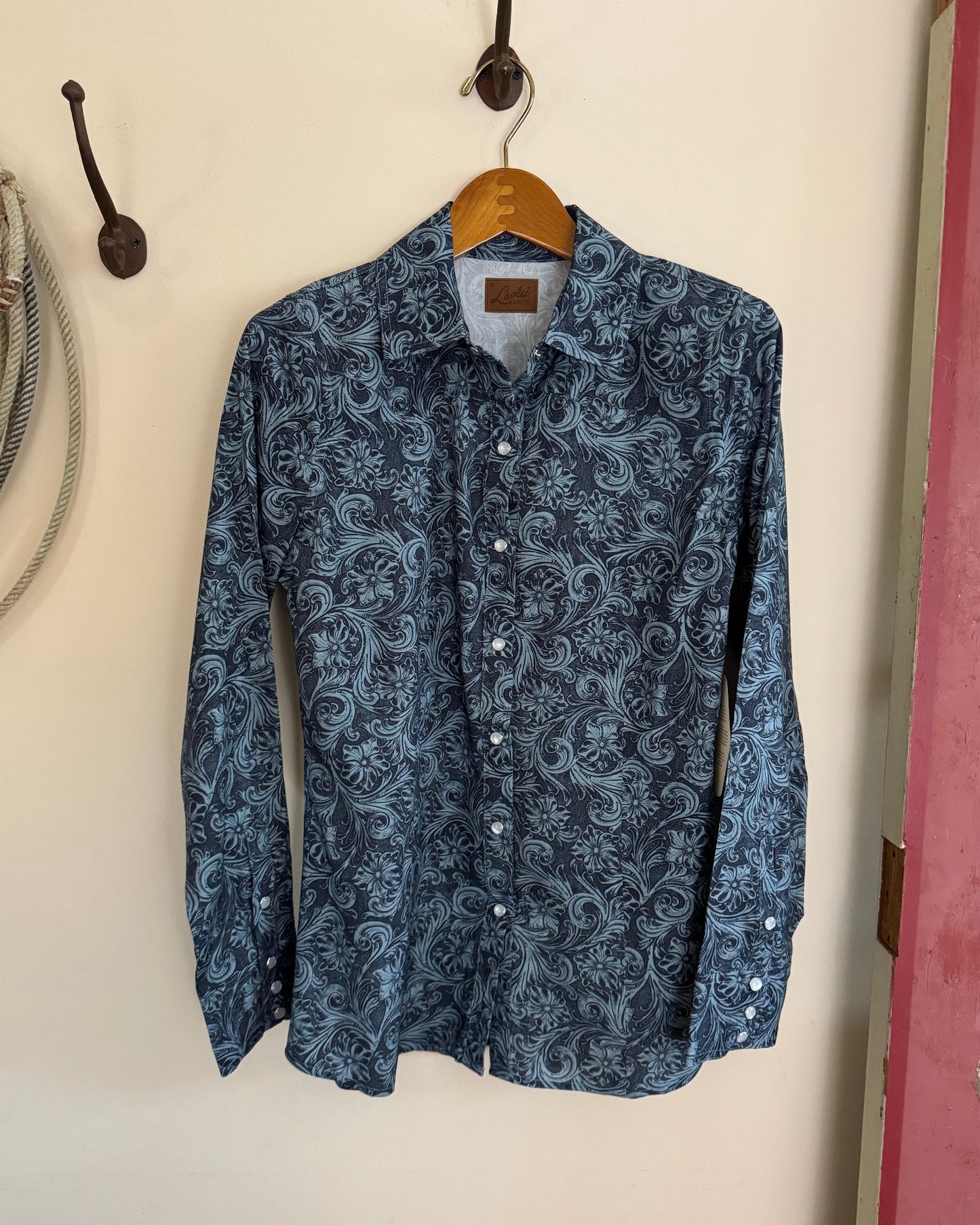 Blue patterned shirt hanging on a wooden hanger against a white wall.