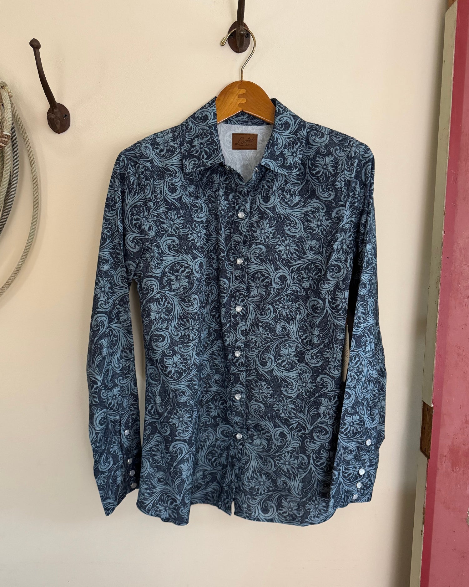 Blue patterned shirt hanging on a wooden hanger against a white wall.