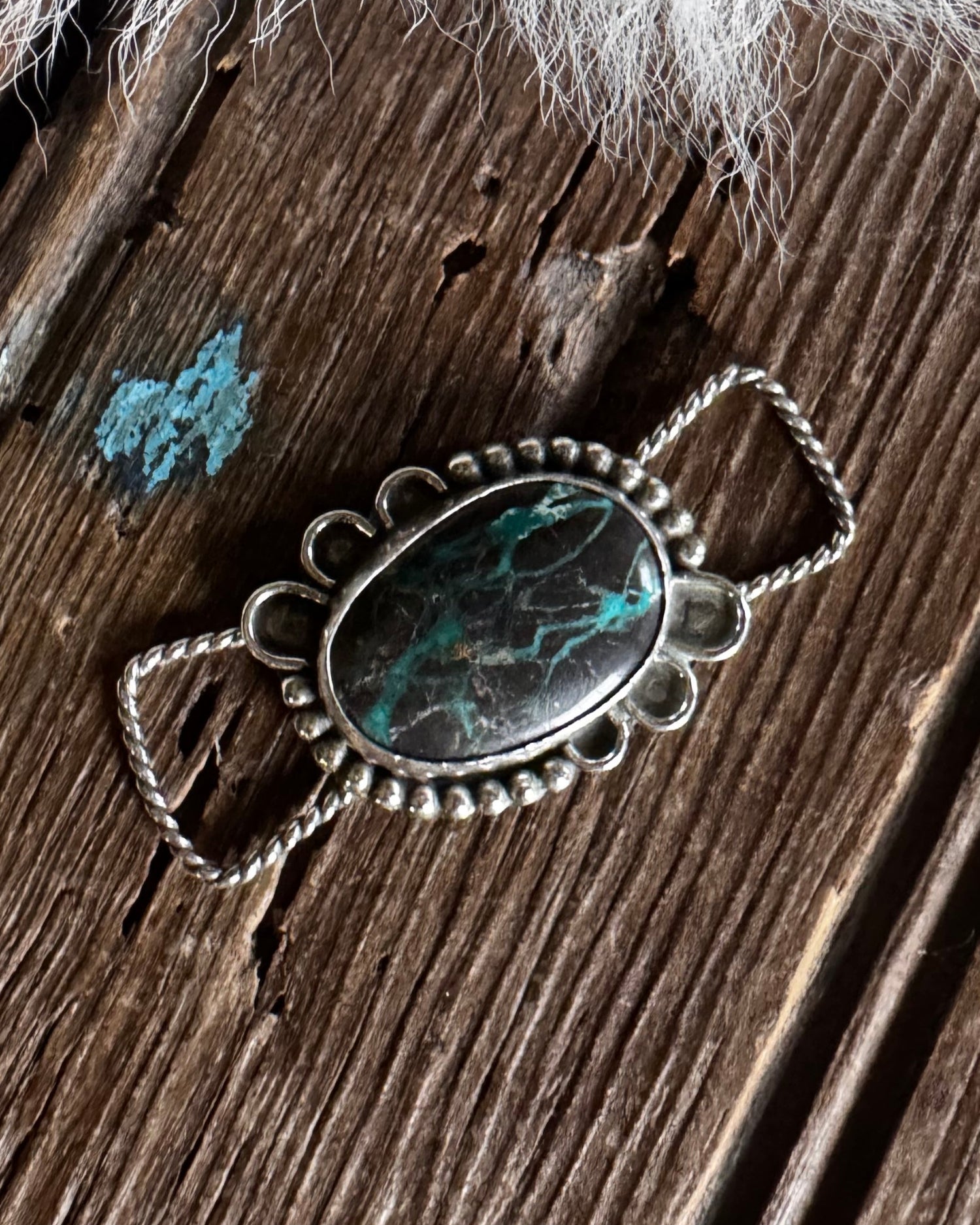 Silver pendant with turquoise stone on a wooden surface with white fur