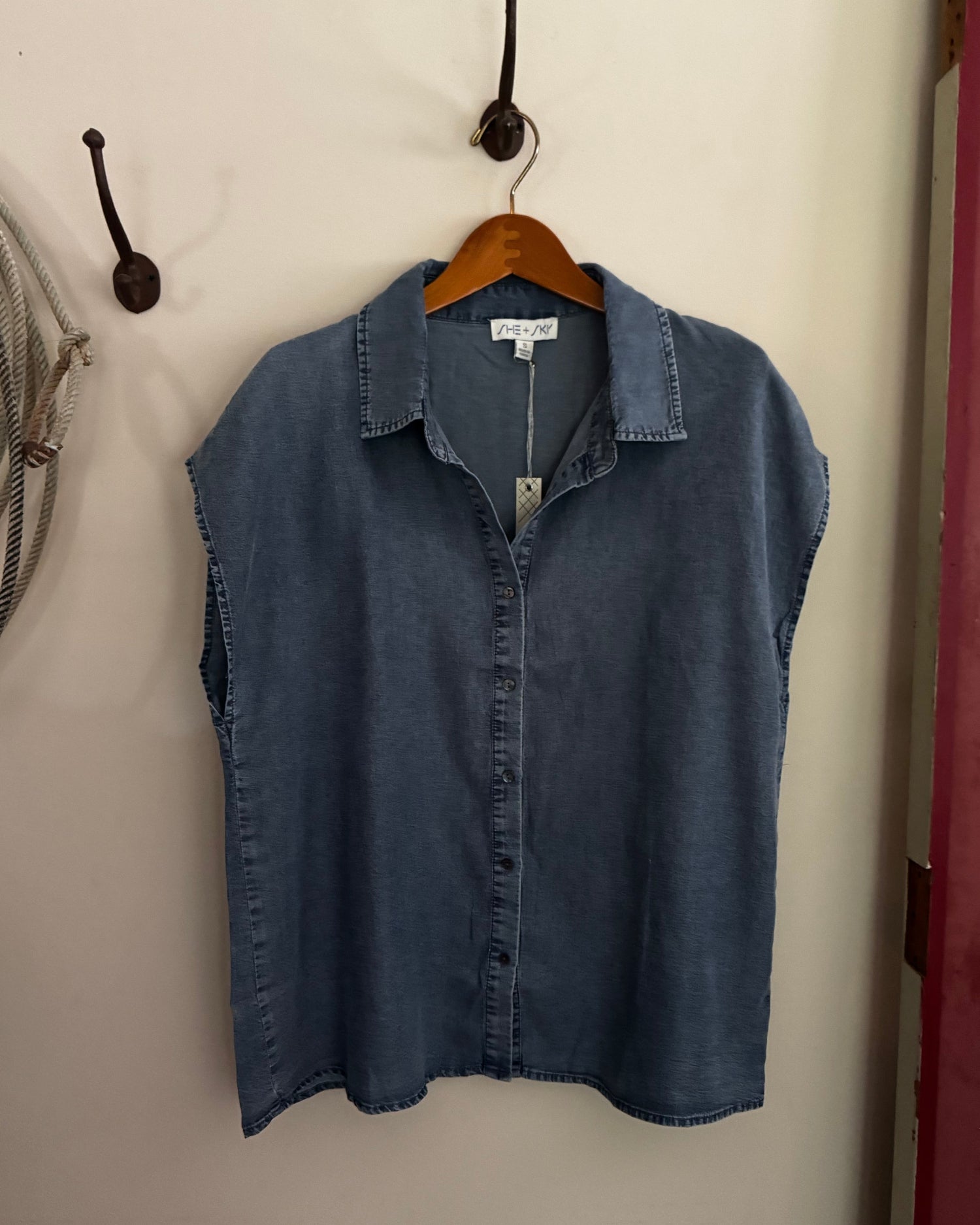 Blue denim shirt on a hanger against a beige wall.
