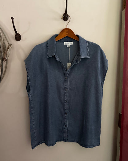 Blue denim shirt on a hanger against a beige wall.