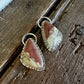 A pair of teardrop-shaped dangle earrings with brown and cream marbled stone in silver bezel settings, displayed on a rustic dark wood surface.