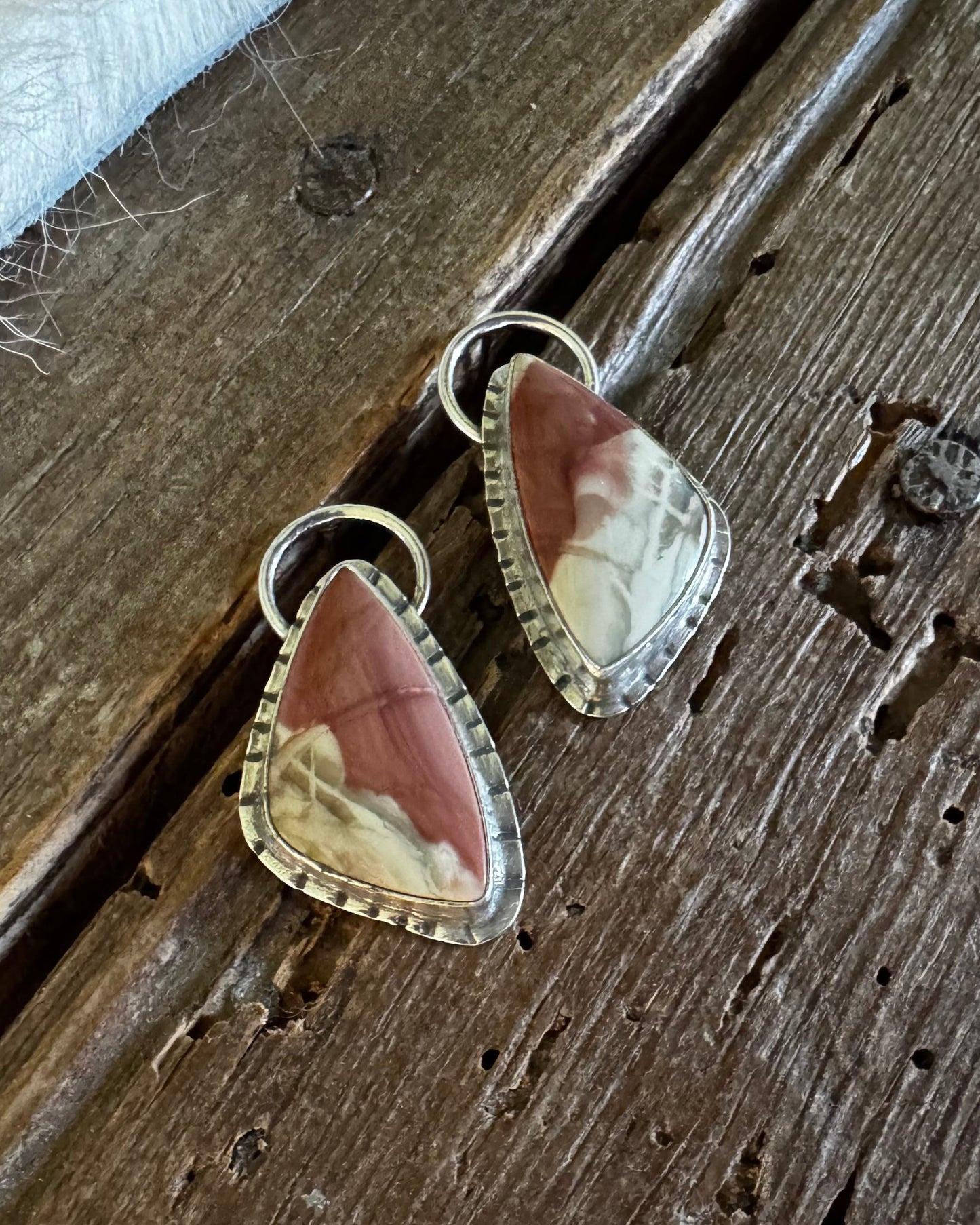 A pair of teardrop-shaped dangle earrings with brown and cream marbled stone in silver bezel settings, displayed on a rustic dark wood surface.
