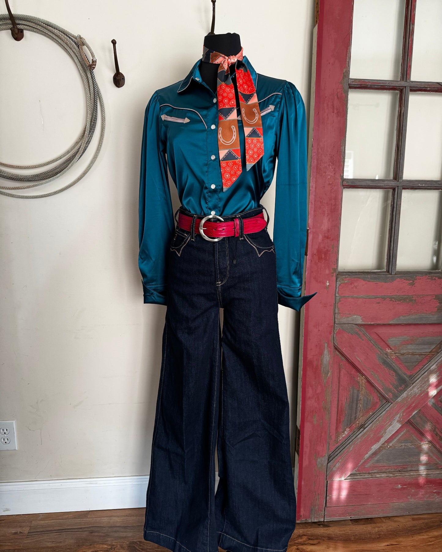 Pair of dark blue pants with a red belt and turquoise blouse with a white background and red door. 
