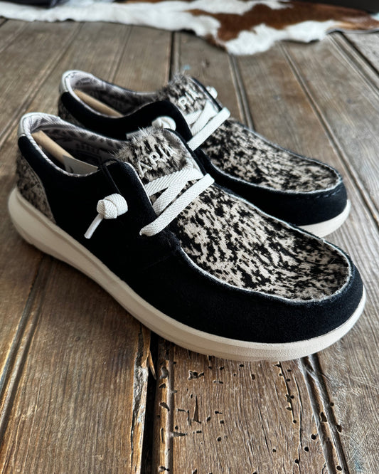 Pair of black and brown sneakers with white laces leaning against a wooden wall.