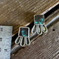 Pair of earrings on a wooden surface with a ruler for scale.