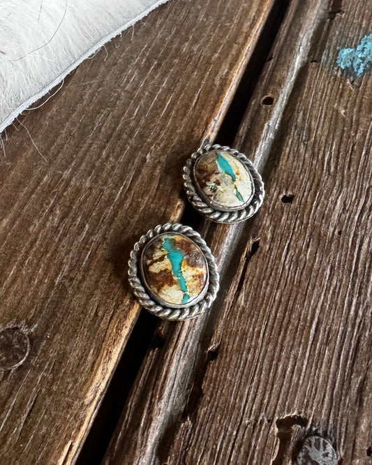 Pair of silver earrings with embedded stones on a wooden surface