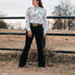 Model standing by a pipe fence in a field, dressed in a stylish modern western outfit.