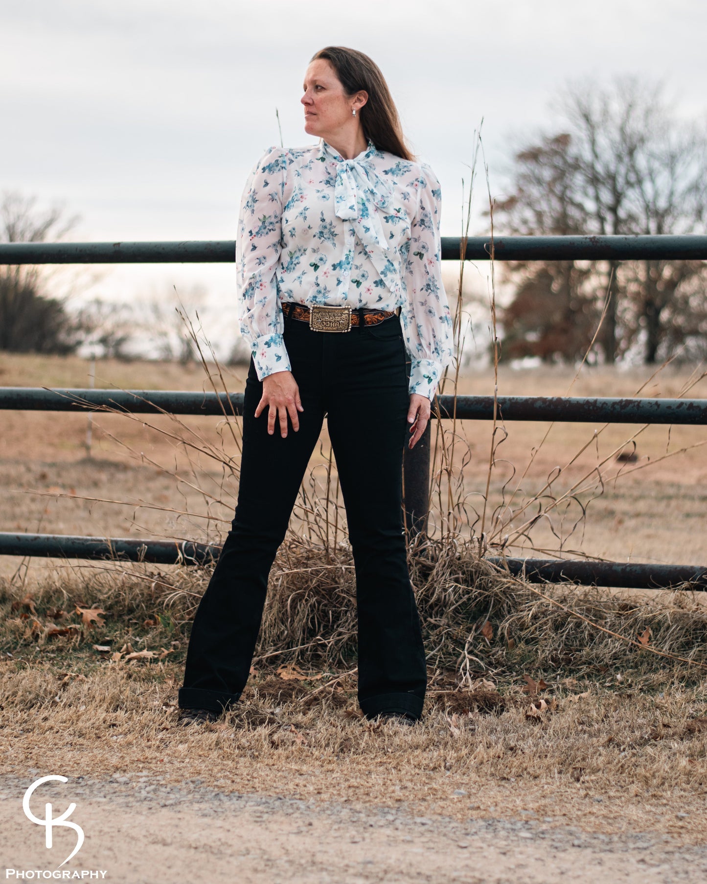 Model standing by a pipe fence in a field, dressed in a stylish modern western outfit.