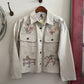 Embroidered jacket hanging on a wall with a wooden hanger.
