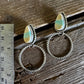 Pair of hoop earrings with heart-shaped charms on a wooden surface with a ruler for scale.