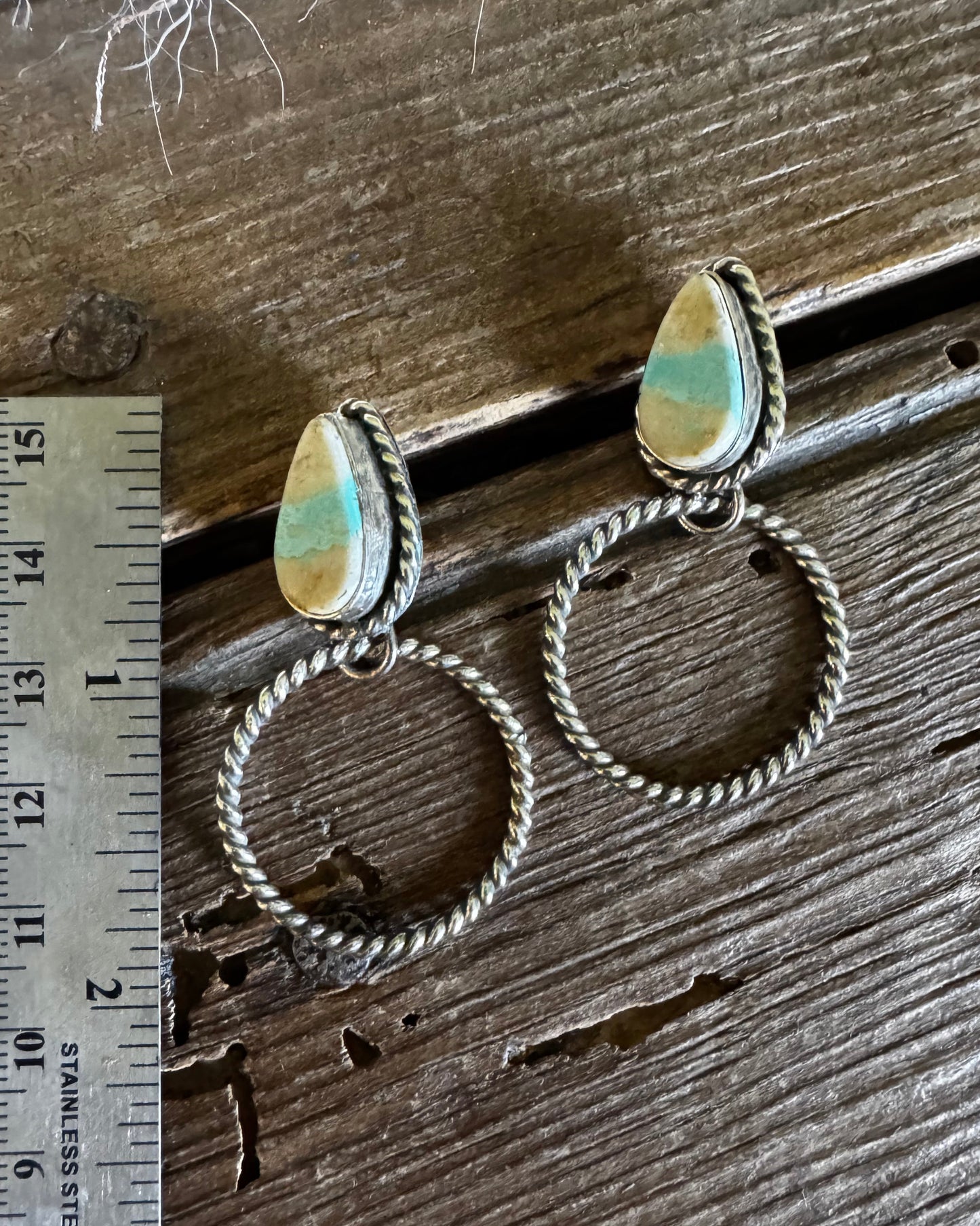 Pair of hoop earrings with heart-shaped charms on a wooden surface with a ruler for scale.