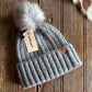 Gray knit beanie with pom-pom and Ariat tag on a wooden surface
